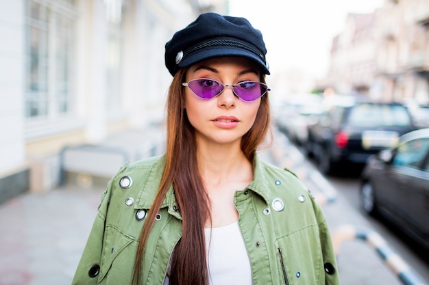 Foto grátis brincalhão mulher posando ao ar livre. usando óculos retrô roxos na moda, boné preto