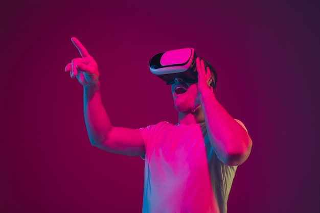 Brincando com VR, atirando, dirigindo. Retrato de homem branco isolado na parede rosa-roxa do estúdio.