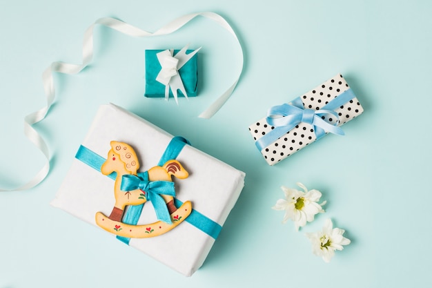 Brinquedo de cavalo de balanço com caixas de presente; flores e fita sobre o pano de fundo azul
