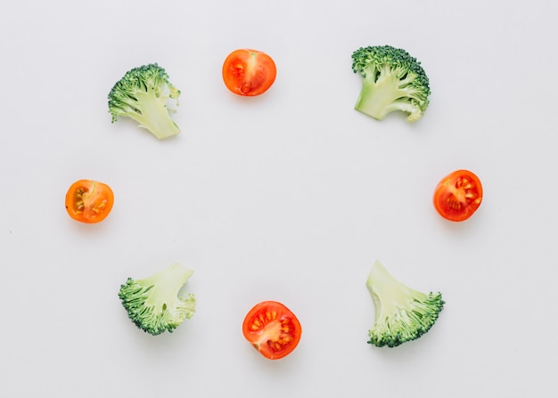 Brócolis pela metade arranjados e tomates cereja no quadro circular isolado no fundo branco