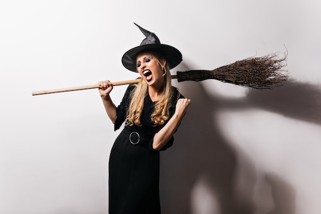 Bruxa encantadora em roupa preta, curtindo a festa. incrível assistente loiro com vassoura.