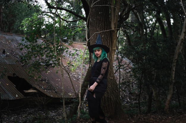 Bruxa jovem perto do tronco da árvore