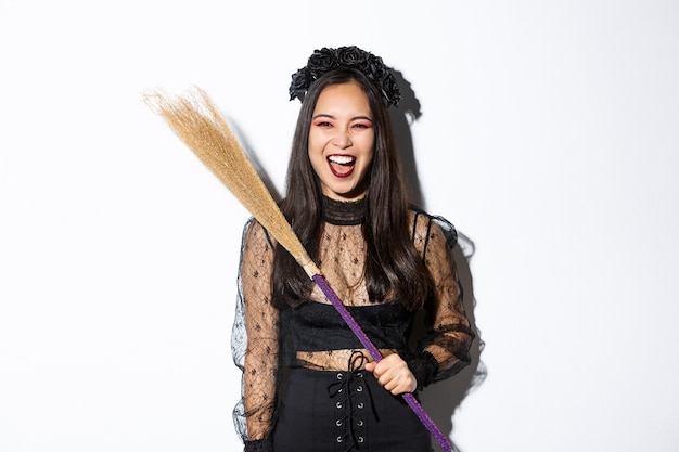 Foto grátis bruxa malvada rindo e acenando com sua vassoura, usando fantasia de halloween