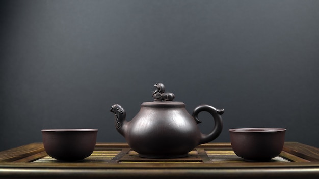 Bule de chá antigo e duas tigelas de barro em uma superfície de madeira