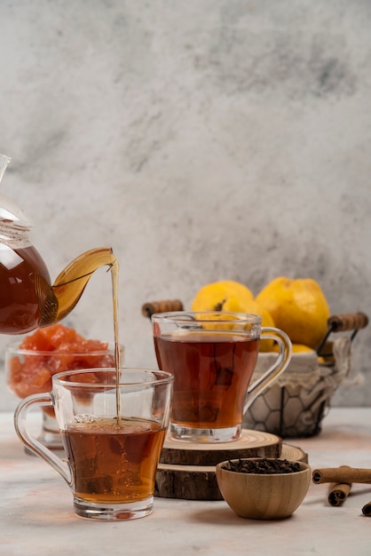 Bule de vidro transparente derrama chá na caneca de vidro na mesa de mármore.