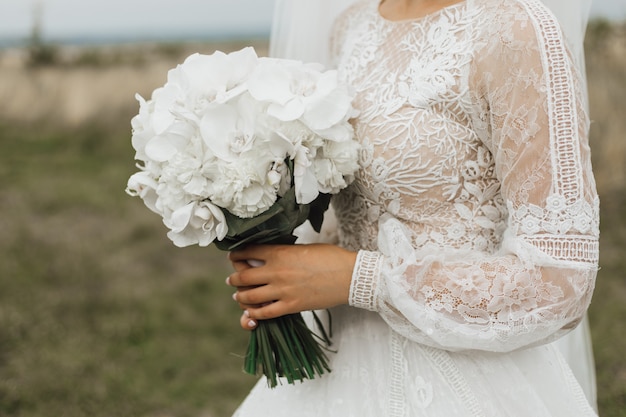 Buquê de casamento feito de peônias brancas na mão da noiva ao ar livre