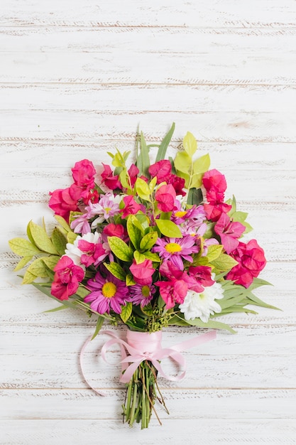 Buquê de flores coloridas amarrado com fita rosa na mesa de madeira