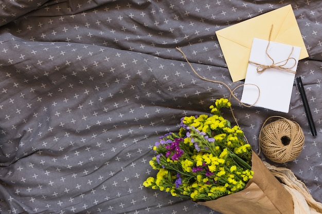 Foto grátis buquê de flores coloridas com carretel de seqüência de caracteres; cartão; caneta e envelope em têxtil cinza