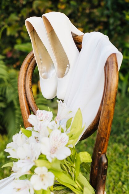 Buquê de flores de casamento; saltos altos e lenço na cadeira de madeira no parque