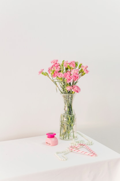 Buquê de flores em um vaso perto de bastões de doces, caixa e contas na mesa