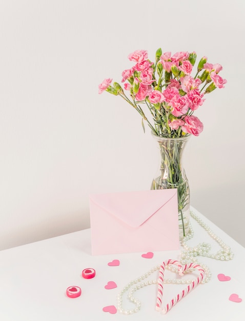 Buquê de flores em um vaso perto de bastões de doces, envelope e missangas na mesa