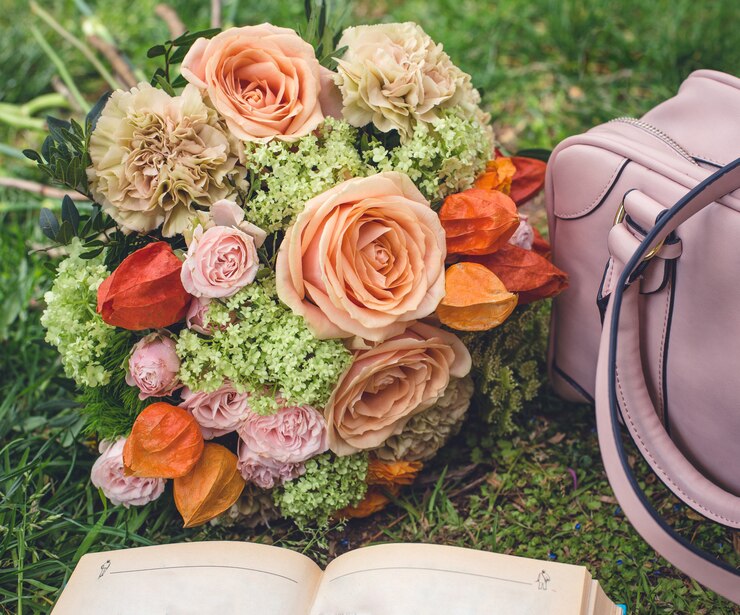 Foto grátis buquê de flores na grama, sacola e um livro