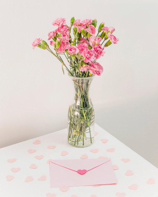 Buquê de flores no vaso perto de envelope e papel corações na mesa