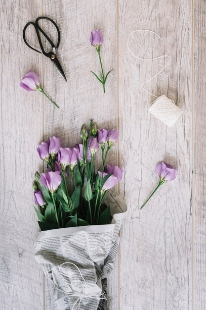 Buquê de flores roxo lindo eustoma com tesoura e carretel branco sobre fundo de madeira