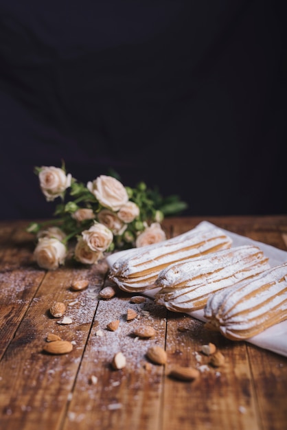 Buquê de rosas com amêndoas e eclairs caseiros no guardanapo sobre a mesa de madeira