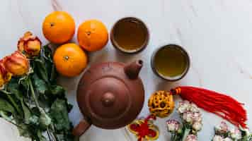 Foto grátis buquê de rosas secas; laranja inteira; borla; bule de barro um xícaras de chá em pano de fundo de mármore