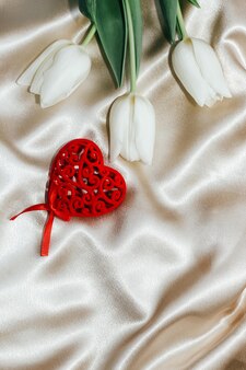 Buquê de tulipas brancas com um coração em um fundo de cetim nude dourado de seda