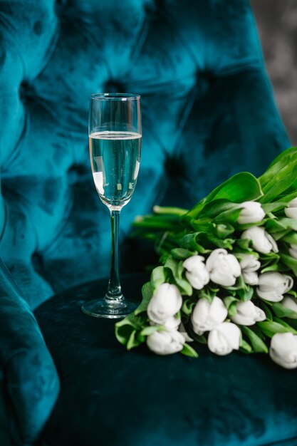 buquê de tulipas flores brancas com uma taça de champanhe em uma poltrona verde