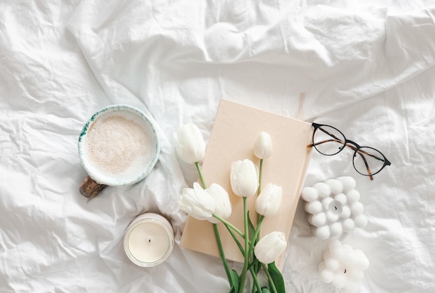 Buquê de tulipas, velas de café e um livro na vista superior da cama