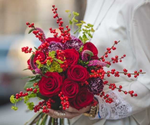 Buquê de veludo vermelho de frutas, flores e flores nas mãos de uma senhora de blusa branca