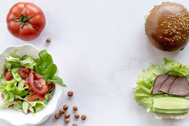 Burger; salada de vegetais; tomate inteiro; avelã sobre a superfície branca