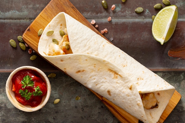 Foto grátis burrito na tábua de cortar perto de molho de tomate, fatias de limão e sementes de cardamomo