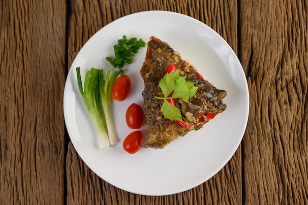 Cabeças de peixe fritas cobertas com pimentões em um prato branco com tomates e cebolinhas.