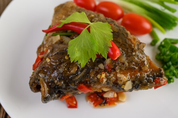 Cabeças de peixe fritas cobertas com pimentões em um prato branco com tomates e cebolinhas.