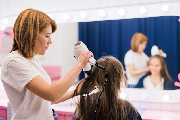 Foto grátis cabeleireira profissional secando o cabelo de mulher usando secador no salão de cabeleireiro