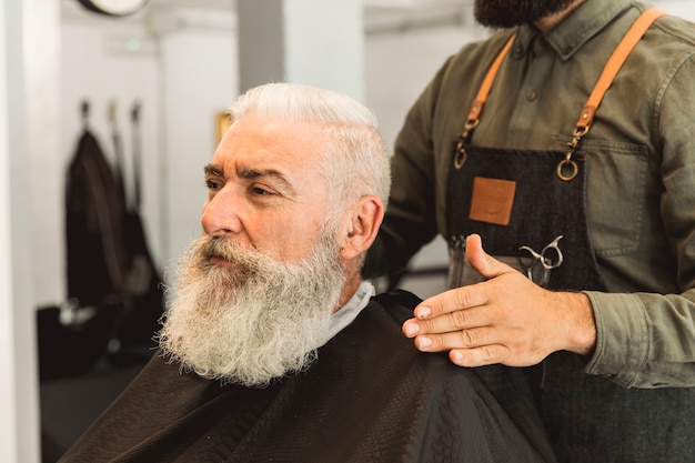 Cabeleireiro avaliando cliente sênior na barbearia