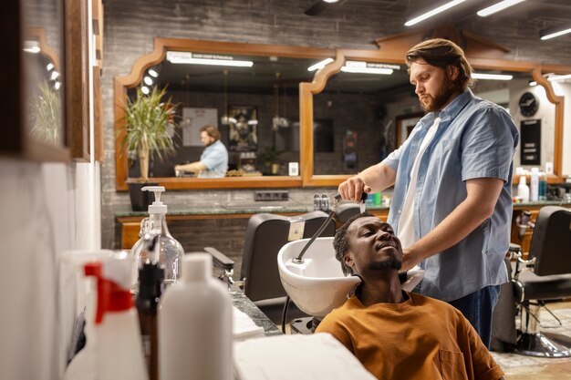 Cabeleireiro de tiro médio lavando o cabelo do homem