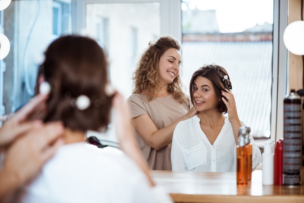 Cabeleireiro feminino e mulher sorrindo, olhando no espelho no salão de beleza