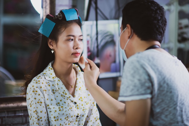 Cabeleireiro feminino em pé, maquiagem de rosto e fazer penteado bonito adorável jovem no salão de beleza