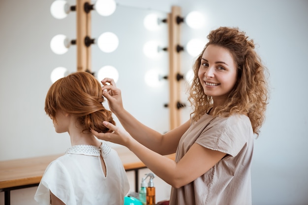 Cabeleireiro feminino sorrindo fazendo penteado para mulher ruiva no salão de beleza
