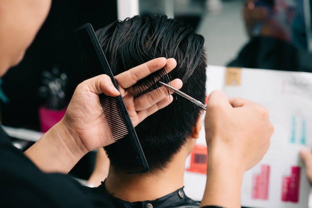 Cabeleireiro irreconhecível, cortar o cabelo do cliente com pente e tesoura no salão