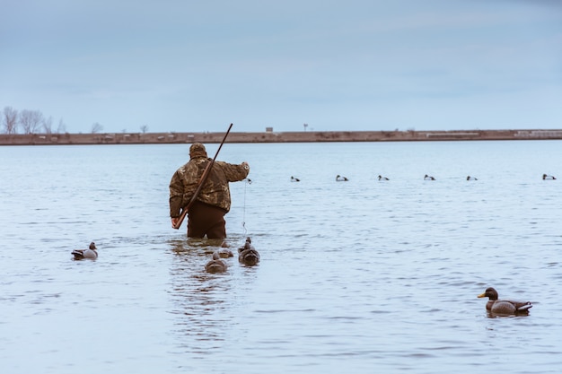 Caçador com um rifle nas costas dando um tempo na caça e pegando um peixe no lago com patos