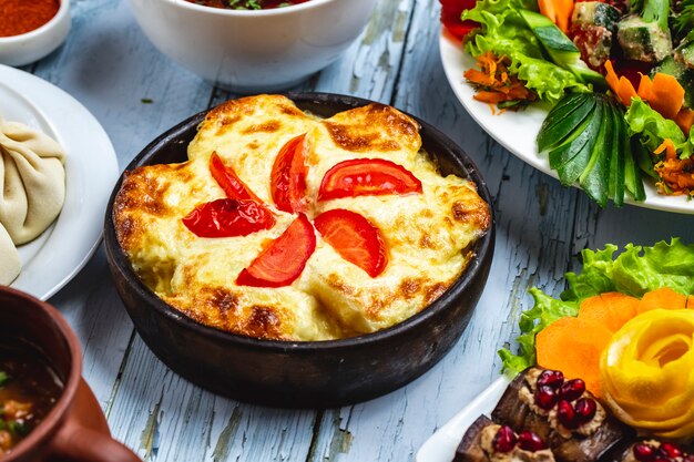 Caçarola de vista lateral com queijo de batata e tomate em um prato de barro