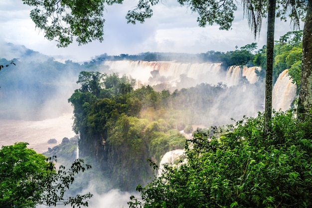 Cachoeira do Parque Nacional do Iguaçu cercada por florestas cobertas pela névoa sob um céu nublado