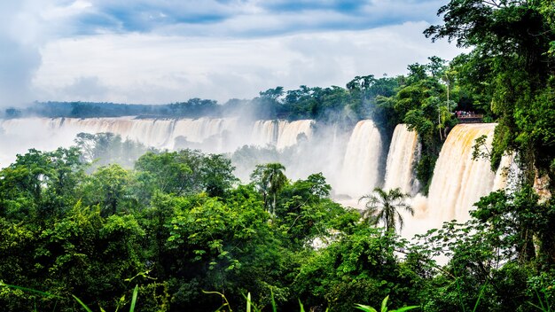 Cachoeira do Parque Nacional do Iguaçu cercada por florestas cobertas pela névoa sob um céu nublado