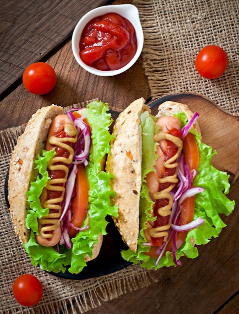 Cachorro-quente com ketchup mostarda e alface na mesa de madeira.