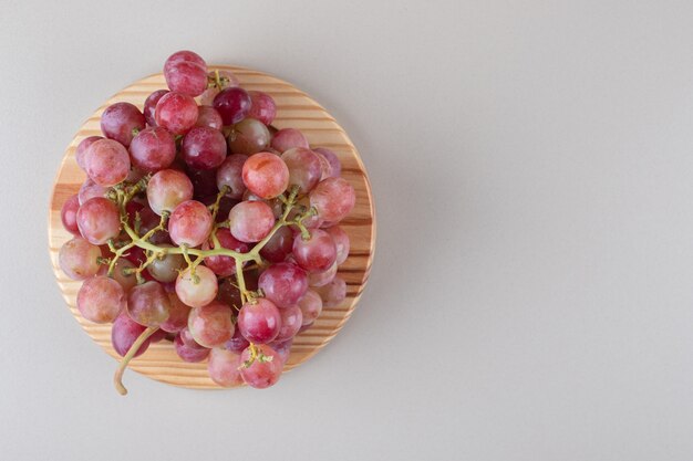 Cachos de uvas vermelhas em uma travessa de madeira sobre mármore