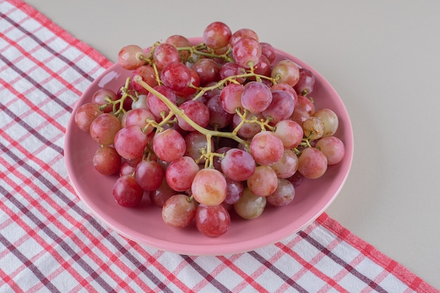 Cachos de uvas vermelhas em uma travessa rosa sobre uma toalha, em mármore