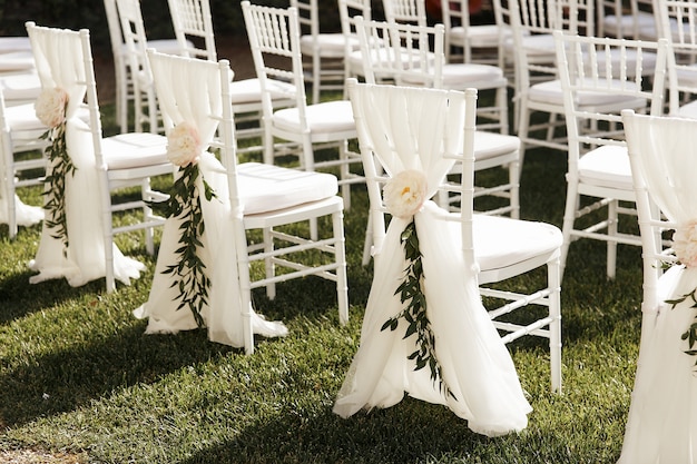 Cadeiras brancas decoradas com peônias e vegetação fora