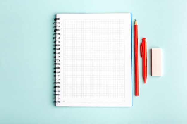 Caderno aberto de vista frontal com caneta e lápis na superfície azul