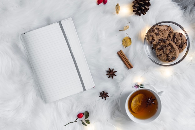 Caderno aberto na manta perto de chá com biscoitos