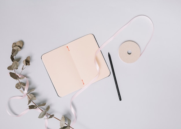 Caderno com pequena ramificação e fita na mesa