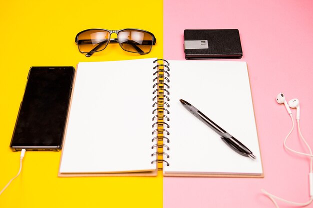 Caderno de papel, smartphone, óculos de sol e suporte para cartões de visita em fundo de duas cores