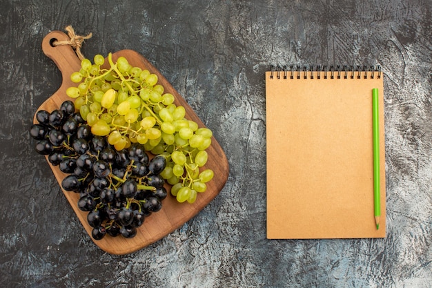 Foto grátis caderno de uvas com vista superior, cachos de uvas verdes e pretas na tábua