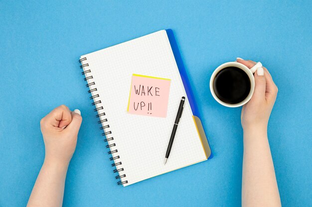 Caderno e xícara de café nas mãos da mulher acordar conceito