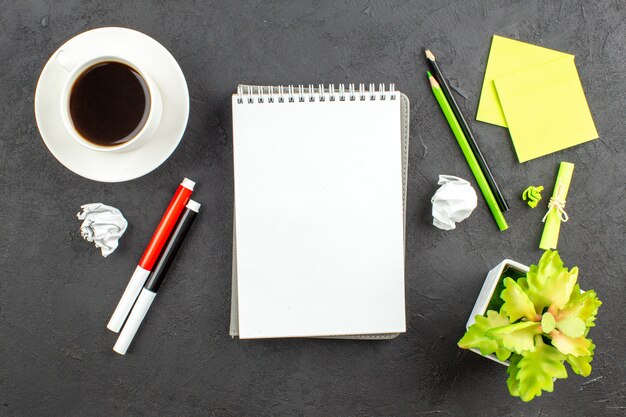 Caderno espiral de vista superior marcadores vermelhos e pretos lápis verde e preto xícara de chá notas adesivas no preto